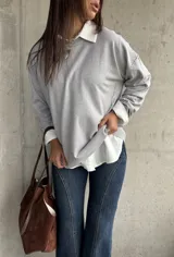 Sweater de punto color gris, de corte holgado y diseño de manga larga con costuras visibles en los hombros. Presenta cuello redondo y puños acanalados.