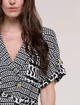 Conjunto de dos piezas de calce fluido y relajado con estampado geométrico en blanco y negro. Incluye una chaqueta con escote en V, solapa, diseño cruzado con lazo y bolsillos con solapa en el pecho, y un pantalón de tiro alto y corte wide leg.