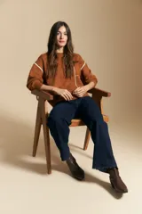 Sweater de punto color marrón con diseño de líneas blancas en contraste. Presenta cuello redondo, mangas largas y puños tejidos, con una estética minimalista y moderna.