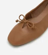Zapatilla tipo bailarina Satinato confeccionada en cuero color tostado, con punta redondeada y detalle de mini lazo en la parte superior. Cuenta con suela plana de baja altura.
