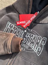 Campera canguro con cierre frontal, capucha y bolsillos tipo canguro, en tono marrón con efecto gastado vintage y estampa gráfica blanca con detalles de strass en el pecho.