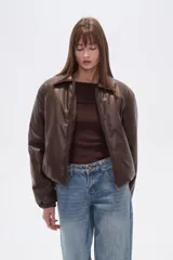 Campera estilo bomber de eco-cuero negra, con cuello camisero, cierre frontal y puños y cintura ajustados con elástico.