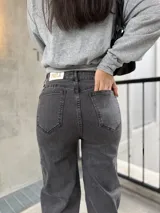 Pantalón de jean color negro lavado, de corte recto y tiro alto. Presenta detalles de tachas metálicas a lo largo de las costuras laterales superiores.