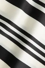 Top asimétrico de satén con diseño de un solo hombro y efecto pañuelo, con patrón geométrico de rayas en blanco y negro.