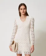 Vestido corto color blanco de encaje macramé con diseño geométrico, escote de pico, mangas largas abullonadas tipo guante con cremallera invisible en el bajo, cierre de cremallera en el lateral, bajo festoneado, forro de muselina de algodón y cinturón extraíble a juego con elástico y hebilla con el logotipo Oval T dorado, de corte recto.