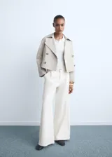 Jeans wide leg de tiro medio color blanco marfil, con diseño largo, trabillas para cinturón, cierre de botón y cremallera, cuatro bolsillos y detalle de pinzas delanteras.