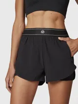 Short deportivo 2 en 1 de color negro, con short interior ajustado y short exterior holgado. Presenta una cintura elástica ancha con detalle de líneas blancas y logo bordado, además de bolsillos laterales invisibles.