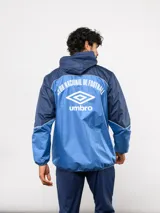 Campera de lluvia Umbro del Club Nacional de Football, con diseño de bloques de color en rojo y azul marino. Presenta capucha, cierre frontal, puños elásticos y detalles de piping blanco. Incluye logo de Umbro y escudo del club en el pecho.