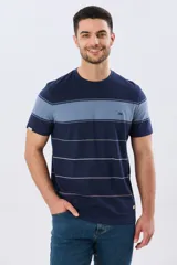 Remera de algodón a rayas, color beige con una franja horizontal ancha en azul marino y líneas finas en azul y verde. Cuenta con cuello redondo y mangas cortas.