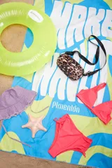 Lona de playa con diseño estampado multicolor, con predominio de azul, verde y blanco, con la inscripción de la marca.