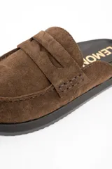 Zueco tipo mocasín destalonado confeccionado en gamuza color marrón, con suela de goma negra y plantilla anatómica.