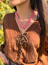 Collar con cadena tejida en hilo rosa y rojo, y dije irregular dorado en forma de flor.