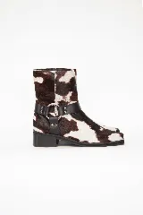 Bota corta de cuero con pelo de vaca en diseño animal print de manchas marrones y blancas, con punta cuadrada, taco bajo y correa de cuero negro con tachas y una argolla metálica alrededor del tobillo.