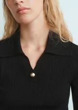 Jersey de canalé color negro, con cuello camisero, manga larga y diseño entallado. Cuenta con detalle de botón efecto joya.
