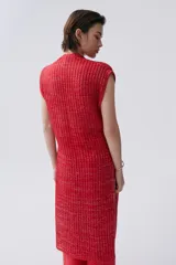 Kimono tejido de punto en color crudo con sutil brillo de lurex. Presenta un diseño sin mangas, corte largo y cierre frontal mediante dos lazos finos. El tejido tiene una textura acanalada vertical.