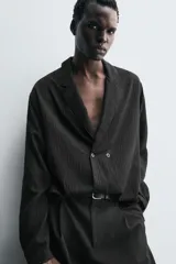 Camisa de corte relajado confeccionada en tejido fluido con mezcla de viscosa. Presenta diseño de rayas verticales sutiles, cuello con solapas de muesca, manga larga con puños abotonados y cierre frontal de botonadura cruzada.