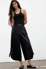 Pantalón culotte de tiro medio, color verde militar, con cintura elástica y bolsillos laterales ocultos. Presenta un diseño de bajo ancho con aberturas ajustables mediante cordones fruncidos en los laterales.