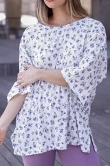 Remera de corte holgado con mangas anchas y aberturas laterales en el ruedo. Presenta un estampado floral pequeño en tonos violeta y verde sobre una base blanca con textura acanalada.