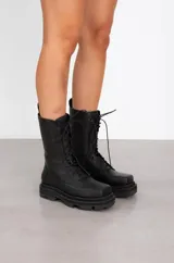 Borcegos de cuero negro con caña media, cierre mediante cordones frontales y suela track robusta con plataforma.