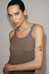 Brazalete rígido de metal dorado con diseño de estructura ondulada y extremos decorados con espirales circulares.