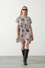 Vestido corto de silueta amplia con corte bajo busto, cuello a la base y mangas cortas. El tejido presenta un estampado de hojas en tonos rojo óxido y turquesa sobre un fondo de rayas verticales blancas y negras.