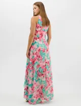 Vestido largo de chifón con estampado floral en tonos rosa y turquesa. Presenta cuello halter con abertura tipo lágrima, cintura drapeada con detalle de nudo central y falda amplia con capas asimétricas. Incluye forro interior y cierre invisible en la espalda.