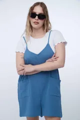 Mono corto de algodón color azul, de corte holgado, con tirantes finos regulables, escote en V y bolsillos frontales aplicados.