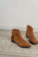 Botas cortas de cuero negro con paneles traseros de gamuza, cierre lateral y detalle de correa con hebilla metálica en el tobillo.
