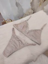 Conjunto de lencería compuesto por un bralette triangular y una bombacha tipo colaless, confeccionados en algodón color nude con delicados detalles de encaje en los bordes.