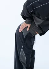 Pantalon deportivo de estilo urbano, confeccionado en tela técnica, con cintura elástica ajustable mediante cordón. Presenta un diseño bicolor en negro y gris oscuro con líneas laterales en contraste.