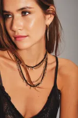 Collar multicapa compuesto por varias cadenas finas que alternan cuentas de vidrio negras y cuentas metálicas doradas, con pequeños dijes colgantes circulares.