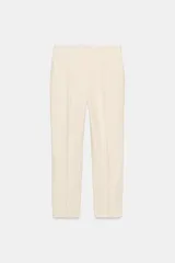 Pantalón color crema de tiro alto con bolsillos delanteros y falsos bolsillos traseros. Tiene una pequeña abertura lateral en el ruedo y cierre frontal con cremallera y gancho metálico.