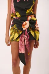 Minifalda negra con estampado floral en tonos amarillo, naranja, rosa y verde. Diseño cruzado con lazo ajustable en la cintura.