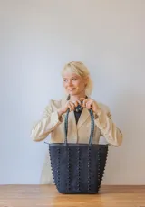 Cartera tipo tote de gamuza color marrón, con correas trenzadas y detalle de piedras naturales incrustadas en líneas verticales. Cuenta con cierre metálico y forro interior de tela.