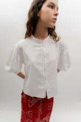 Camisa de lino blanco con lurex, cuello mao, mangas abullonadas y cierre frontal con botones agrupados en pares.