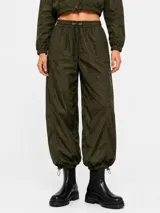 Pantalon estilo parachute verde militar con cintura elastizada ajustable mediante cordón, bolsillos laterales y puños ajustables en los tobillos.