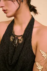 Collar Fenix con cadena dorada, diseño rígido en la parte superior y un gran dije central de inspiración alada con cristales negros.