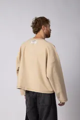 Buzo de cuello redondo confeccionado en tejido rústico con bordes al corte y costuras expuestas. Presenta un diseño boxy con estampado frontal y es reversible, permitiendo su uso por ambos lados.