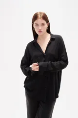 Camisa de corte holgado con estampado de rayas verticales en tonos bordó y blanco. Presenta cuello clásico, cierre frontal con botones, mangas largas con puños abotonados y un bolsillo frontal en el pecho.