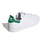 Championes Adidas Stan Smith blancos de cuero, con detalles verdes en el talón y la lengüeta. Diseño clásico con perforaciones laterales y suela de goma.