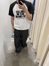 Remera oversize de corte raglan, color blanco con mangas y cuello en contraste negro. Presenta estampado frontal con la inscripción "KILLING IN THE NAME OF" y el texto secundario "NOW YOU DO WHAT THEY TOLD YA".