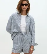 Camisa de jeans de manga larga con estampa de rayas verticales en tonos azul y blanco, cuello inglés, cierre frontal por botones y bolsillos grandes en el frente.