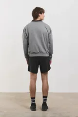 Buzo de algodón rústico color gris melange, con cuello redondo y cuello tipo polo negro superpuesto. Presenta el logo de la marca bordado en el pecho y puños acanalados.