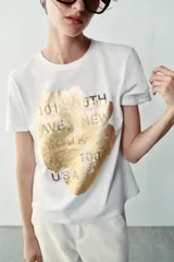 Camiseta blanca de manga corta y cuello redondo, con detalle de estampa central metalizada de efecto texturizado y diseño regular fit.