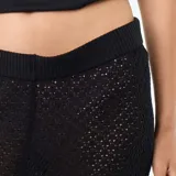 Pantalón de playa color negro, confeccionado en tejido de croché con patrón calado, de tiro medio y corte ancho en las piernas.