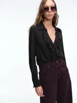 Camisa negra de manga larga con cuello camisero y detalle de volados en la parte frontal. Presenta cierre frontal con botones y puños con abertura.