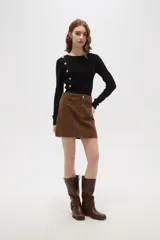 Falda mini de corte recto confeccionada en pana de algodón color verde oliva, con cierre frontal de botón metálico y pasacintos.