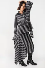 Camisa de corte holgado con estampado de cuadros en tonos marrones y beige. Presenta cuello clásico, cierre frontal con botones y mangas largas con aberturas laterales que permiten anudar la prenda en la cintura.