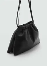 Bolso de hombro pequeño en piel ovino color negro, con diseño fruncido en la parte superior y asa ajustable con hebilla metálica.