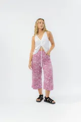 Pantalón culotte de tiro medio con estampado de hojas blancas sobre fondo rosa viejo. Presenta un corte recto y amplio, con cintura elástica en la parte posterior y bolsillos laterales.